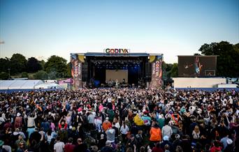 The Godiva Festival stage, branded with banners on each side and above, infornt of a large crowd of people.