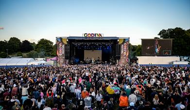 The Godiva Festival stage, branded with banners on each side and above, infornt of a large crowd of people.